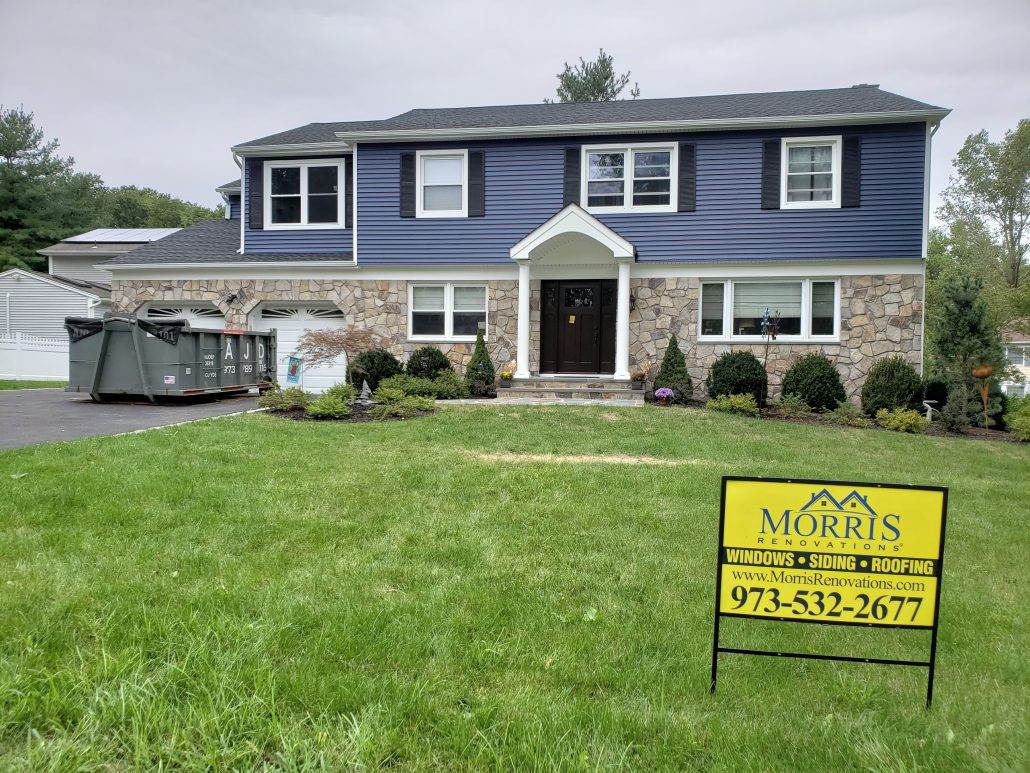 Colonial style house with deep dark blue color vinyl traditional clapboard siding in Whippany NJ Morris County white window trim and white corners morris renovations job sign in front of the house