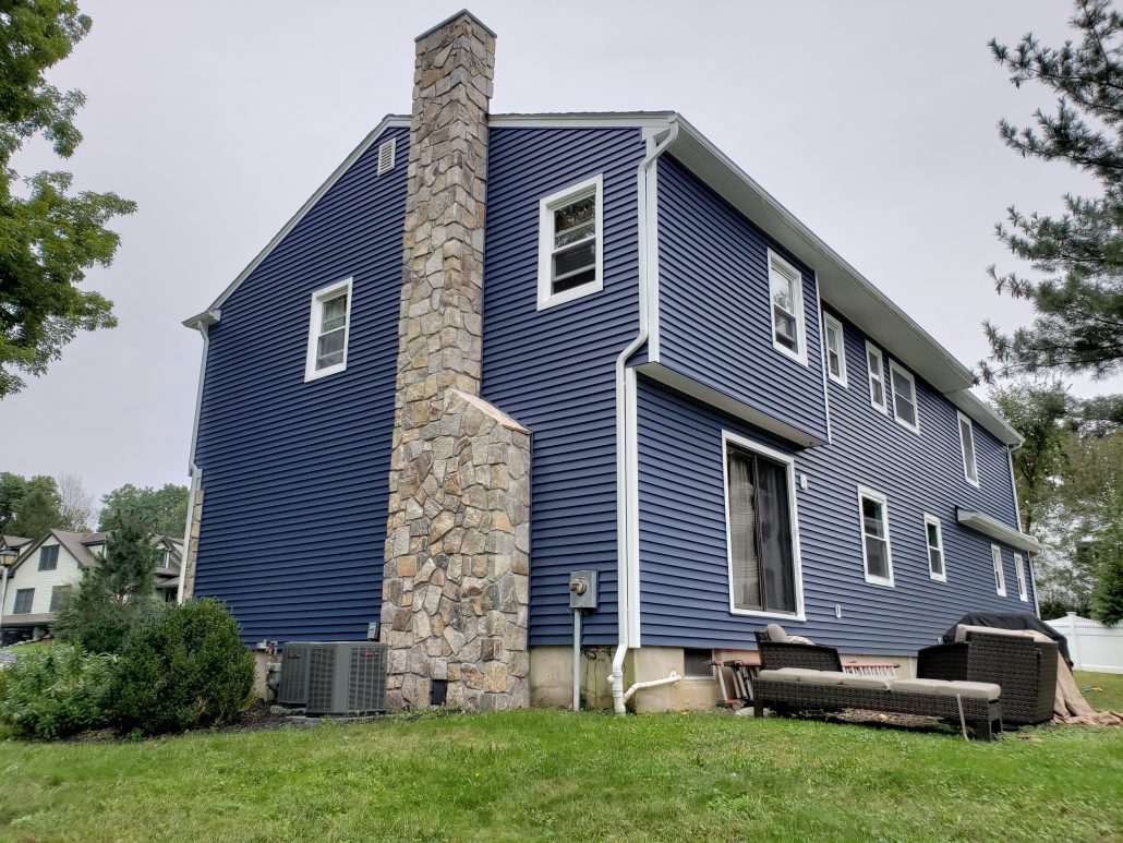 Right side of Colonial style house with deep dark blue color vinyl traditional clapboard siding in Whippany NJ Morris County white window trim and white corners