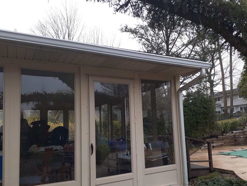 Section of new 5 inch gutter installed on sunroom. Gutters and leaders are white color.
