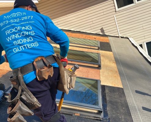 Worker on a roof installing a skylight along with flashing kit and roof shingles